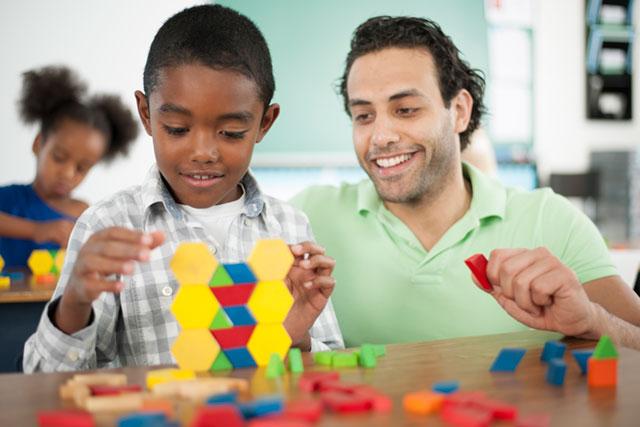 Male teacher helping young student to play with  blocks.