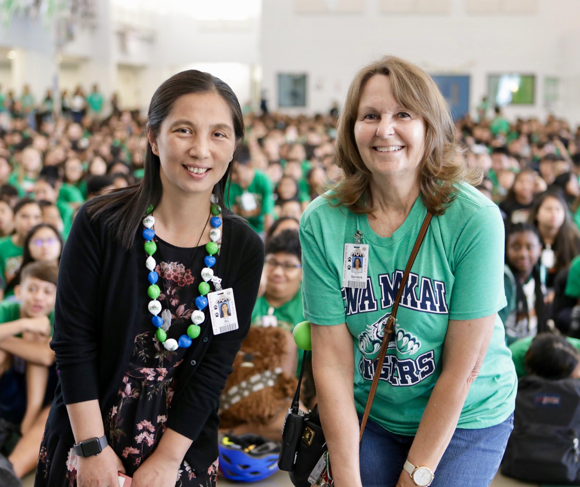 Two teachers in front of a large assembly of students